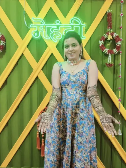 A client posing in front of a neon "Mehndi" sign at her ceremony. Her full-arm designs look absolutely stunning.