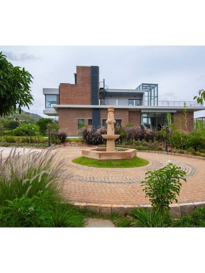 The entrance of the Nandi Hills weekend home, designed with a minimalistic, contemporary style. The circular driveway and central fountain are surrounded by landscaping that blends with the natural environment.