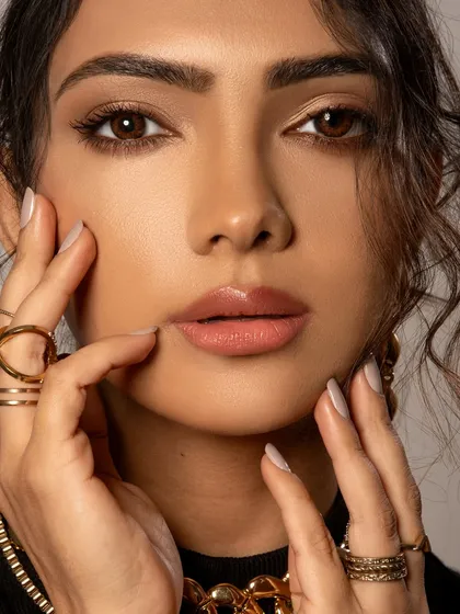 A soft and intimate beauty portrait. The styling is minimal to draw attention to the model's features and the delicate gold rings, creating a natural and elegant look.