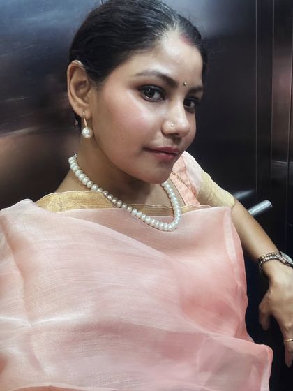 A close-up portrait showcasing the beauty of simple, elegant styling for festive occasions. The pearl earrings and necklace perfectly complement the soft hue of the saree, creating a look of classic sophistication.