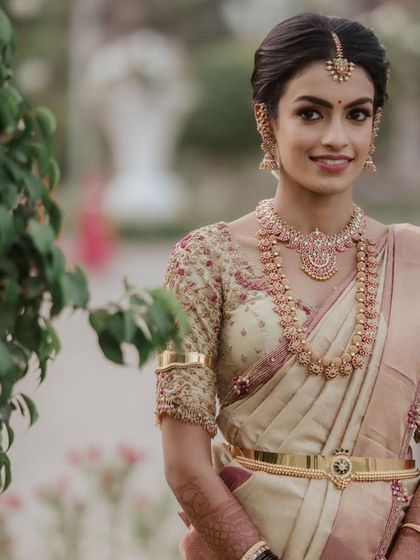 A full portrait of the bride, showcasing the beautiful drape of her silk saree. The intricate gold embroidery on her blouse sleeves adds a layer of regal sophistication.