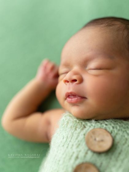 A close-up of a nine-day-old newborn's face, showing their delicate features and soft skin. The light green outfit adds a fresh, natural feel.