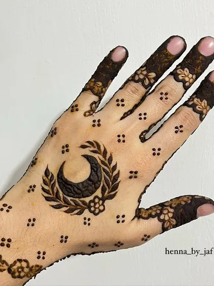 A bold Eid design with a large crescent moon surrounded by a leafy wreath. The hand is covered in a delicate pattern of dots and flowers.