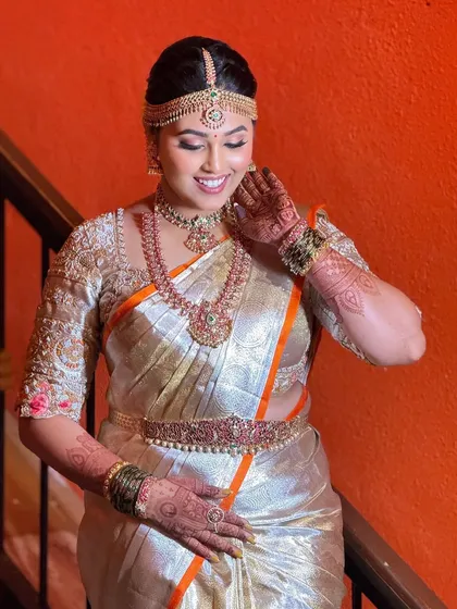 A happy bride in a beautiful silver Kanjeevaram with an orange border. The makeup is fresh and bright, with a focus on glowing skin and a warm smile.