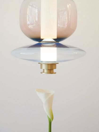 An artistic shot pairing a colorful Luna pendant with a delicate Calla lily, emphasizing the light's sculptural and organic qualities.