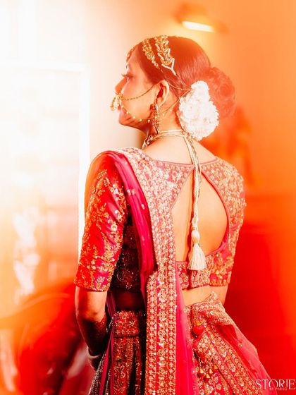 A dreamy bridal portrait with a creative light leak effect. The focus is on the back of her intricately embroidered blouse and her traditional hair accessories, creating a warm and ethereal image.