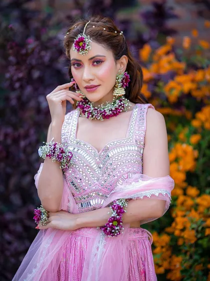 A modern Haldi look with a twist. This model wears a pink lehenga with stunning purple and white floral jewellery, paired with pink-toned eye makeup.