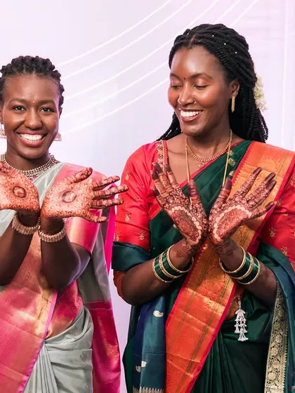 Two women joyfully showing off their beautiful henna designs at a wedding.