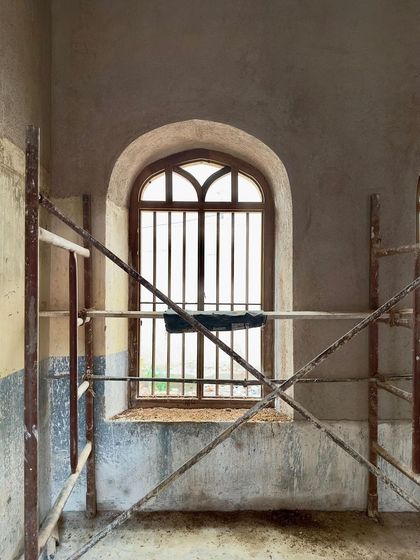 An arched window seen from inside a room under restoration. The scaffolding creates a temporary geometry, framing the view and highlighting the window's elegant form.