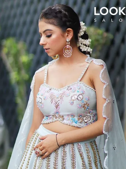 A model looking ethereal in a light blue lehenga, with a braided hairstyle adorned with flowers. This is a perfect look for a daytime wedding or festive event.