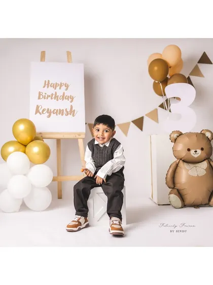 A happy three-year-old boy posing for his birthday portrait with a teddy bear theme.