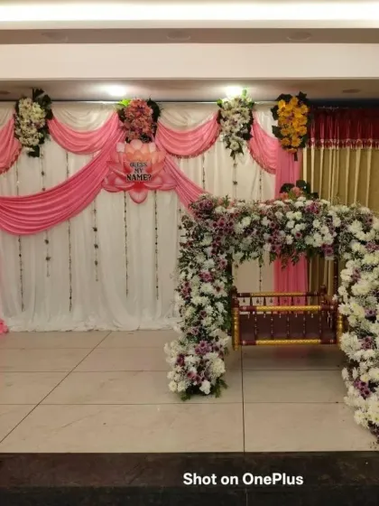 For this naming ceremony, I used a combination of pink fabric drapes and a stunning floral arch over the cradle. The cascading flowers in white and purple add a touch of playful elegance to the stage.