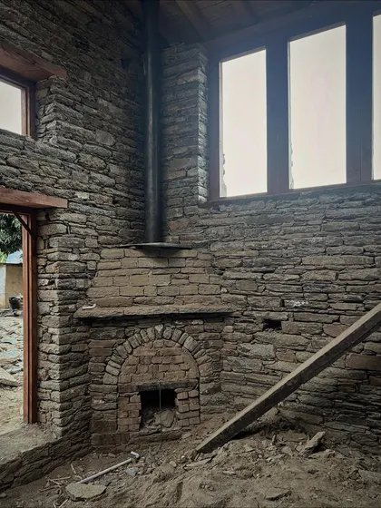 The interior of a restored village home in Uttarakhand, featuring a traditional fireplace built from local stone and brick. We preserve and integrate existing structures whenever possible, honoring the history and craft of the region.