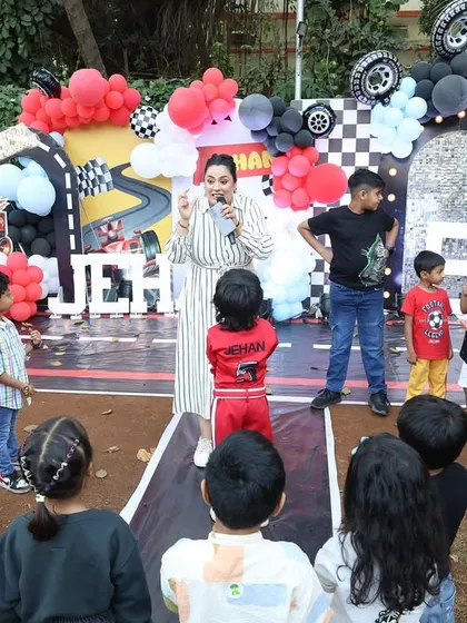 A party host gets the kids excited for a game in front of the race car backdrop. Organized entertainment is key to a smooth and fun party.