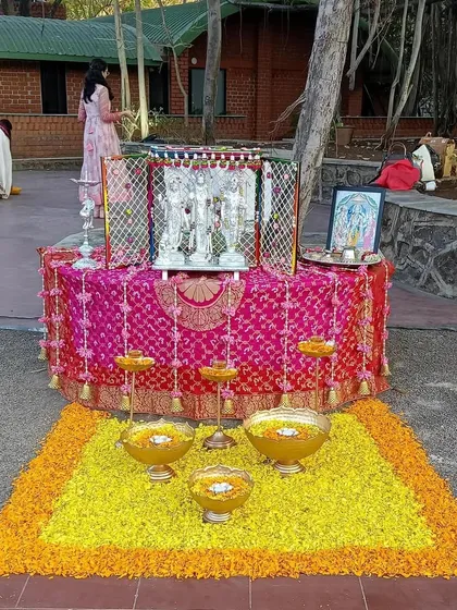 This setup for a Ram Ayodhya Kalash function creates a serene space for prayer. It features a floral mat of marigold petals, brass urlis with floating candles, and a beautifully draped altar for the deities.