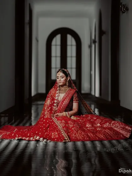 A dramatic shot of the bride seated in a grand corridor, her red lehenga spread out around her.