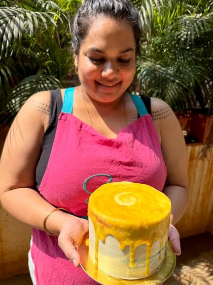 Me, holding one of my creations, a bright yellow drip cake. The smile is genuine because I truly love what I do.