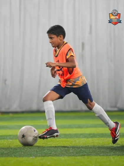 A player in an orange bib dribbles forward during a practice match, applying his skills in a game situation.