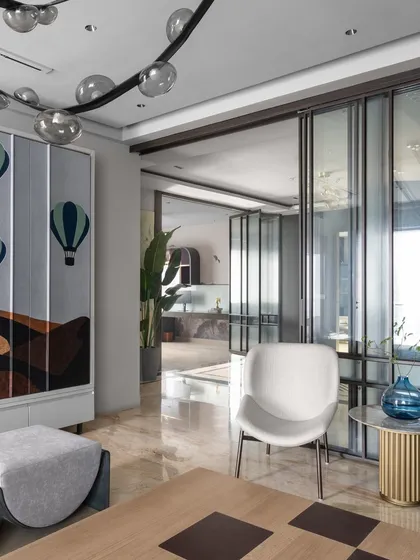 This view shows the transition from the living area to other parts of the loft, framed by a sleek glass partition. The hot-air balloon artwork on the cabinet adds a whimsical touch to the modern design.