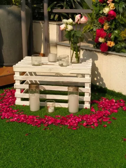 Detail of the decor, showing candles placed on a rustic white crate surrounded by a heart made of red rose petals on the grass.