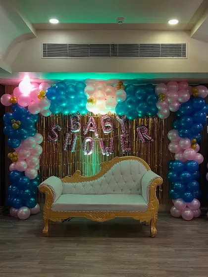 A beautiful baby shower setup with pink and blue balloon arches, "Baby Shower" foil balloons, and an elegant diwan for the parents-to-be.