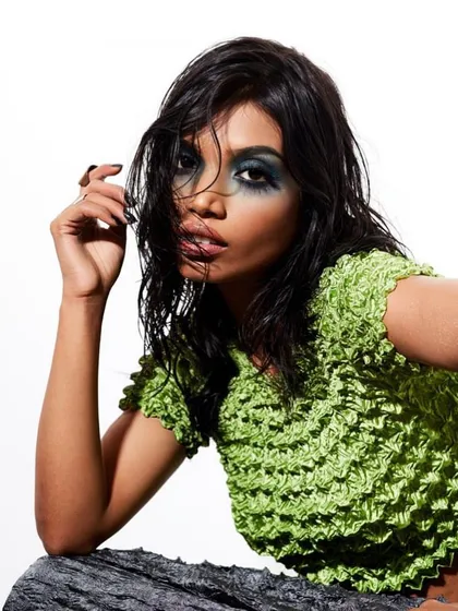 A close-up from an editorial shoot with a focus on a heavy, smudged blue-green smokey eye. The wet-look hair is styled away from the face to emphasize the bold makeup.