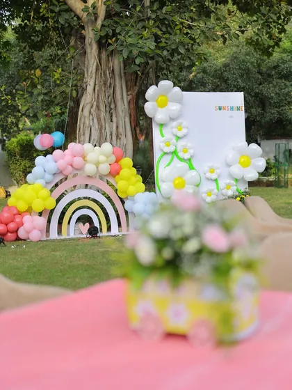 A beautiful shot of the sunshine party setup, with a themed floral centerpiece in the foreground and the main rainbow and daisy backdrop in the background, showing the depth of the decor.