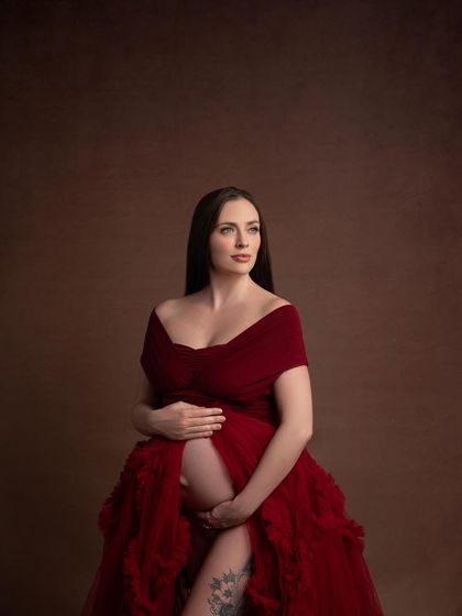 A beautiful close-up portrait, focusing on the mother's expression and the rich texture of the red gown. Her visible tattoo adds a layer of personal story to the image.