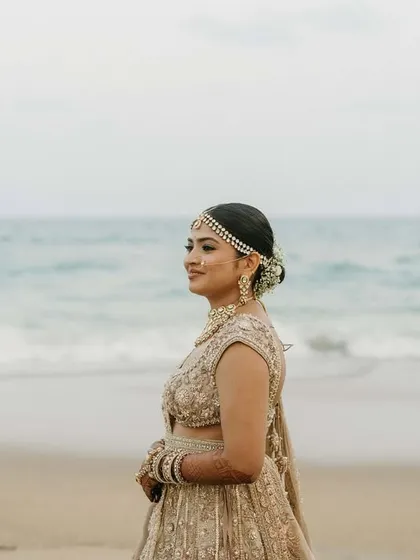 For the serene beach wedding, we created a soft and subtle look. This bride looks ethereal with a neat floral bun, a delicate matha patti, and makeup that complements the calm ocean backdrop.
