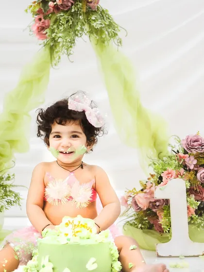 A sweet smile from the birthday girl, surrounded by a lovely green and pink floral setup. The number '1' prop clearly marks this important milestone.