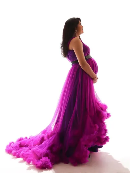 This side profile highlights the beautiful shape of the baby bump against the flowing purple and pink ruffled gown. It's a perfect blend of elegance and drama.