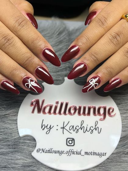 A bold and beautiful deep red set on stiletto nails, with accent nails featuring delicate, hand-painted white bows.