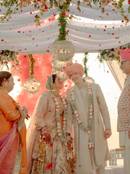 Pure joy and celebration under the mandap. The couple shares a laugh as confetti and smoke fill the air, surrounded by their happy family.