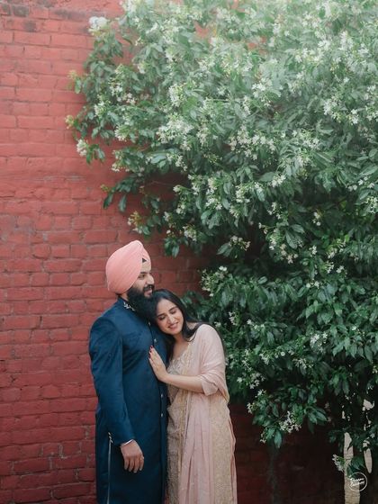 A tender embrace against a rustic wall, framed by a flowering tree. This shot from their Amritsar pre-wedding session is a perfect blend of rustic charm and natural beauty.