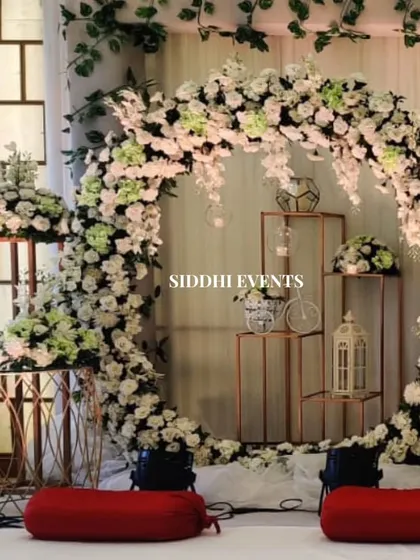 A large circular arch made of white and light green florals creates a stunning focal point, with decorative stands and lanterns adding to the whimsical, garden-like feel.
