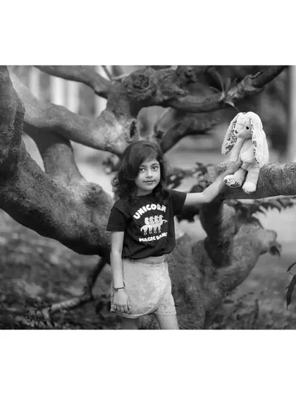 A black and white portrait of Brishka posing with her toy bunny near a tree. The monochrome edit gives the image a timeless, storybook quality.