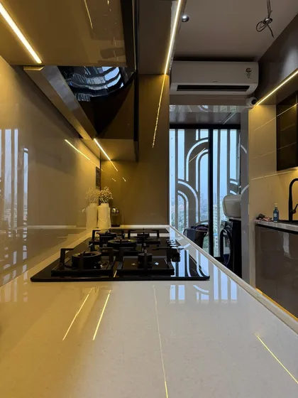 This shot captures the full length of the galley kitchen, showing the sleek chimney hood and the reflection of the profile lighting on the glossy surfaces, which helps make the space feel larger.