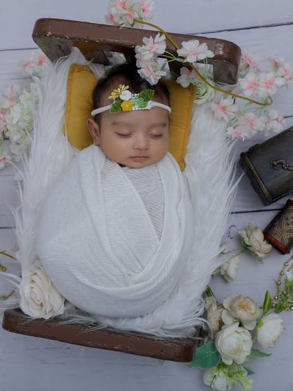 A serene portrait of a newborn baby sleeping in a small wooden crate, surrounded by flowers. We use simple, natural props to keep the focus on your baby's peaceful expression.