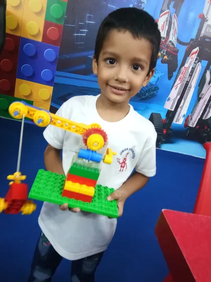 A young student smiles as he shows off the simple machine he built: a working LEGO crane. This demonstrates how we introduce basic mechanical concepts like gears and pulleys.