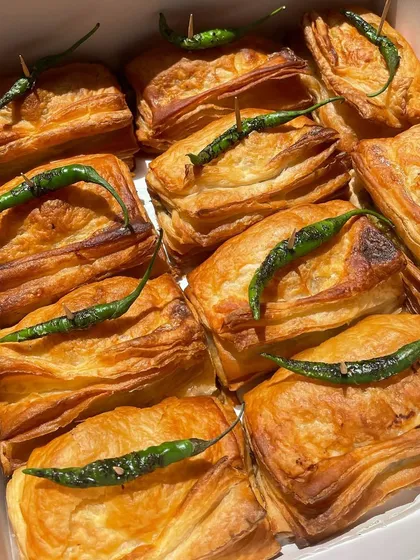 A box full of freshly baked Vada Pav Puffs, each topped with a fried green chili. These are perfect for party platters and I offer a Jain version too.