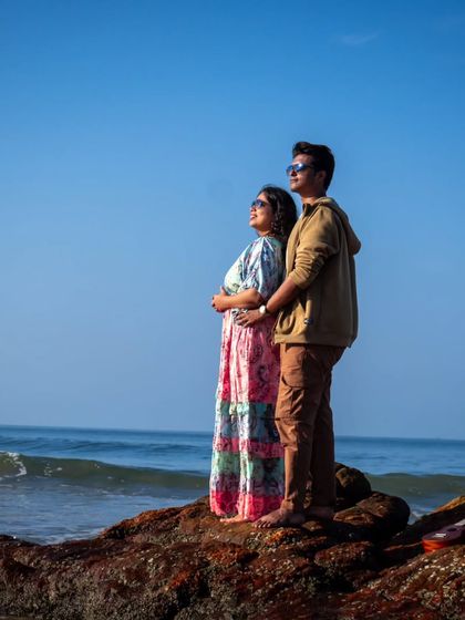 The couple stands together on a rock, looking out at the vast ocean. This pose creates a sense of shared dreams and looking towards the future together, a powerful theme for a pre-wedding shoot.
