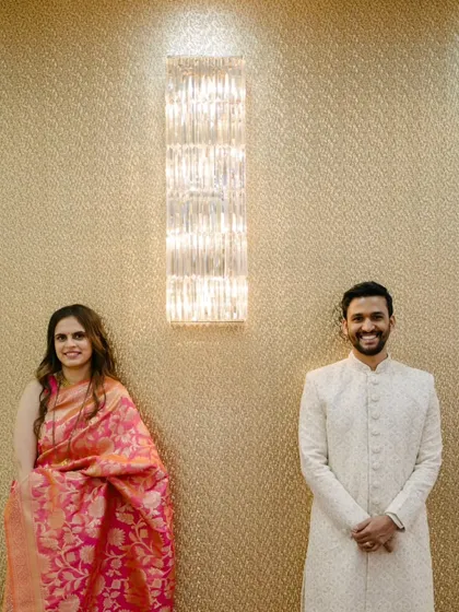 A simple, elegant portrait against a textured gold wall. This shot is about symmetry and quiet confidence, letting their beautiful traditional outfits and happy expressions shine.