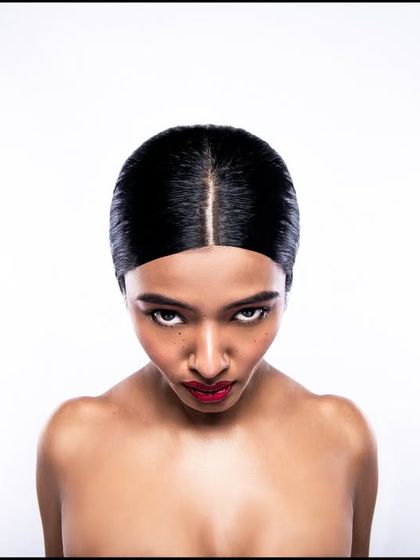 A dramatic, high-angle shot that adds an editorial edge to a commercial beauty campaign. The model's direct, intense gaze combined with the sleek hair and bold red lip creates a powerful and memorable image. This angle is unconventional and designed to grab attention.