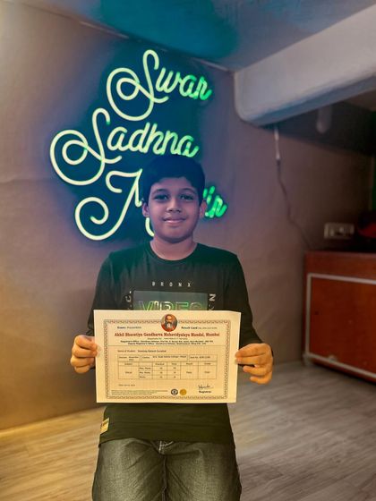 A student proudly holds his certificate against our studio's neon sign. Each certificate represents a step forward in their musical journey.