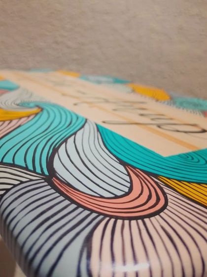 An edge-on view of the "Natya and Anup" name plaque, highlighting the smooth finish and the way the colorful line art wraps around the sides.