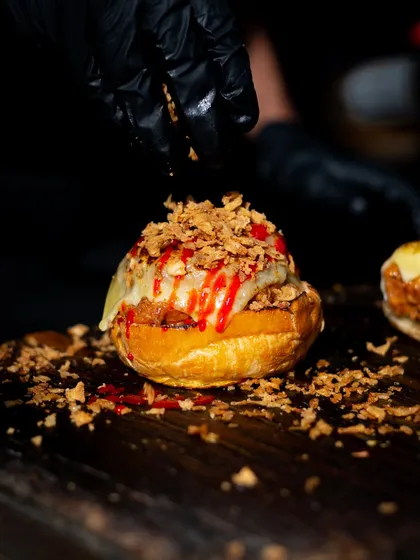 The final touch of crispy onions being sprinkled onto a pulled pork bagel. This image focuses on the texture and generosity of the topping.