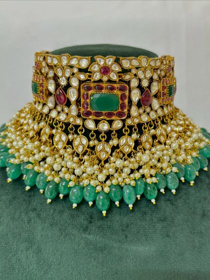 A close-up of a bridal choker with square and teardrop-shaped stones. The green bead border adds a finishing touch to this rental piece.