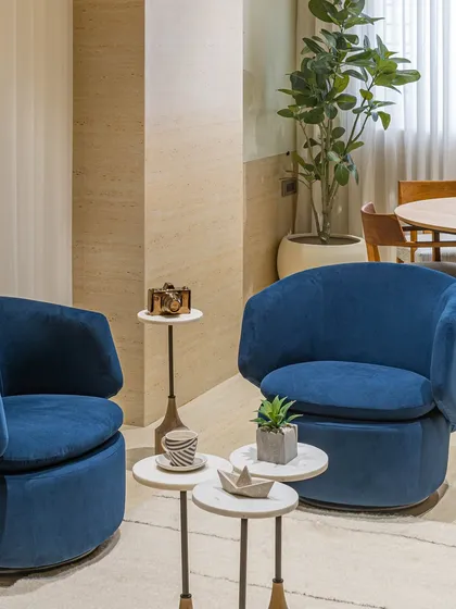 A wider view of the director's lounge area. The vibrant blue chairs serve as a colorful accent against the neutral, earthy tones of the travertine-style walls and wooden furniture.