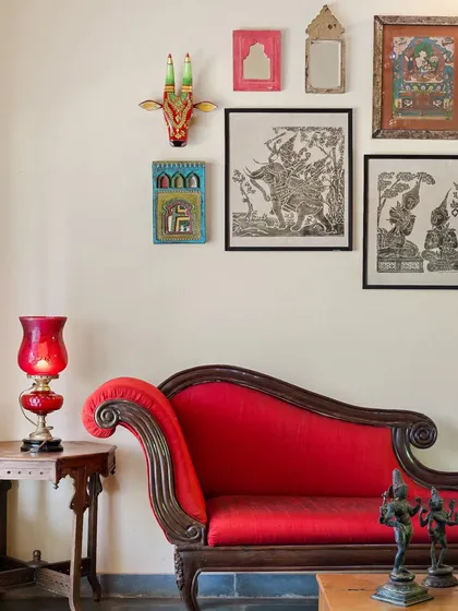A classic red divan sofa, a staple of traditional Indian furniture, adds a bold statement to this living area. The surrounding artifacts and artwork complete the heritage-inspired look.