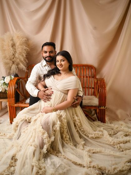 A lovely portrait of the expecting couple seated on a rattan bench. The earthy tones and natural textures of the boho setup create a calm and beautiful scene.